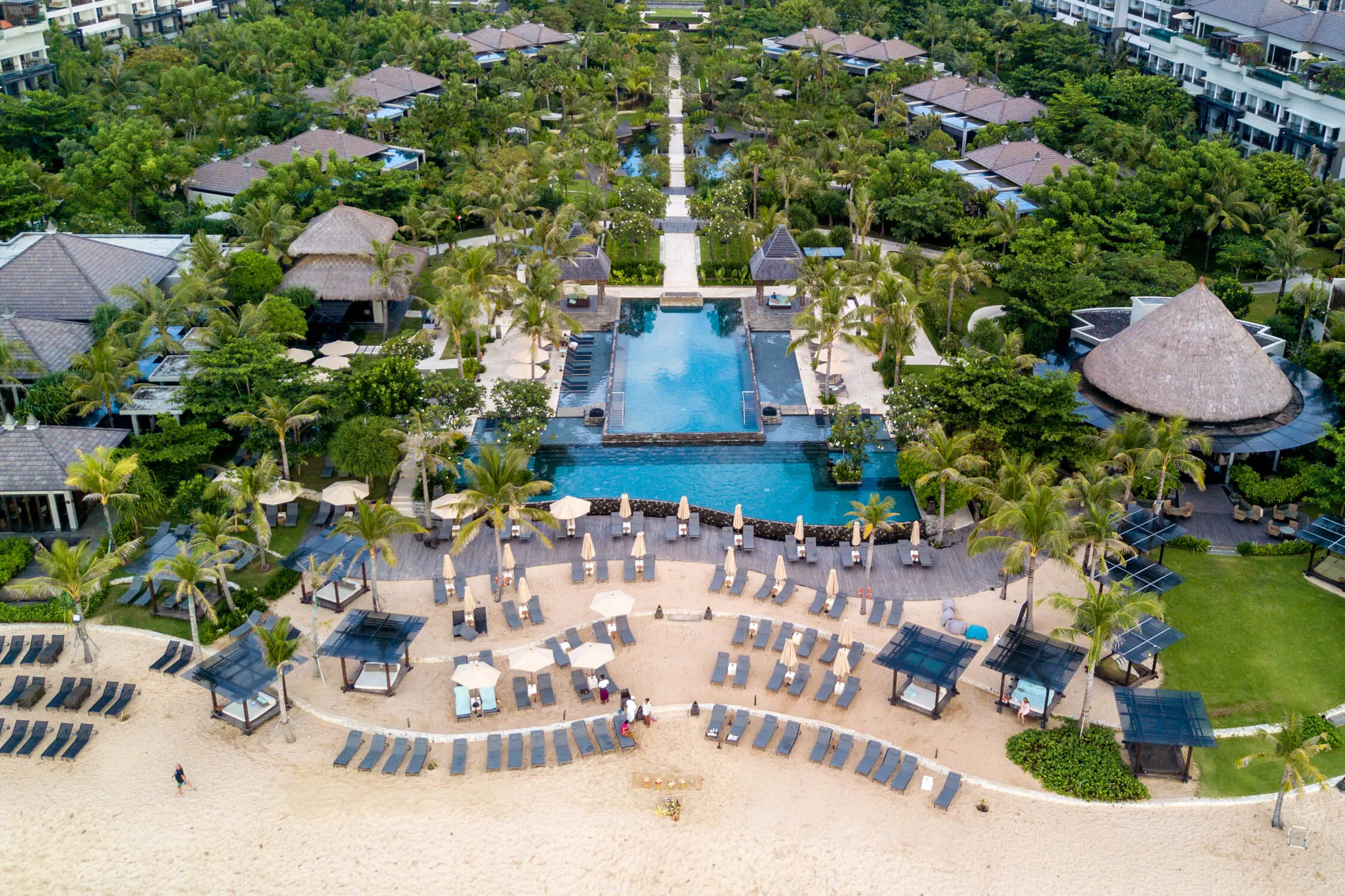 Letecký pohled na resort The Ritz-Carlton na Bali, který se nachází přímo u pláže. Resort je obklopený tropickou zelení, nabízí velký bazén a luxusní relaxační prostory přímo na písečné pláži.