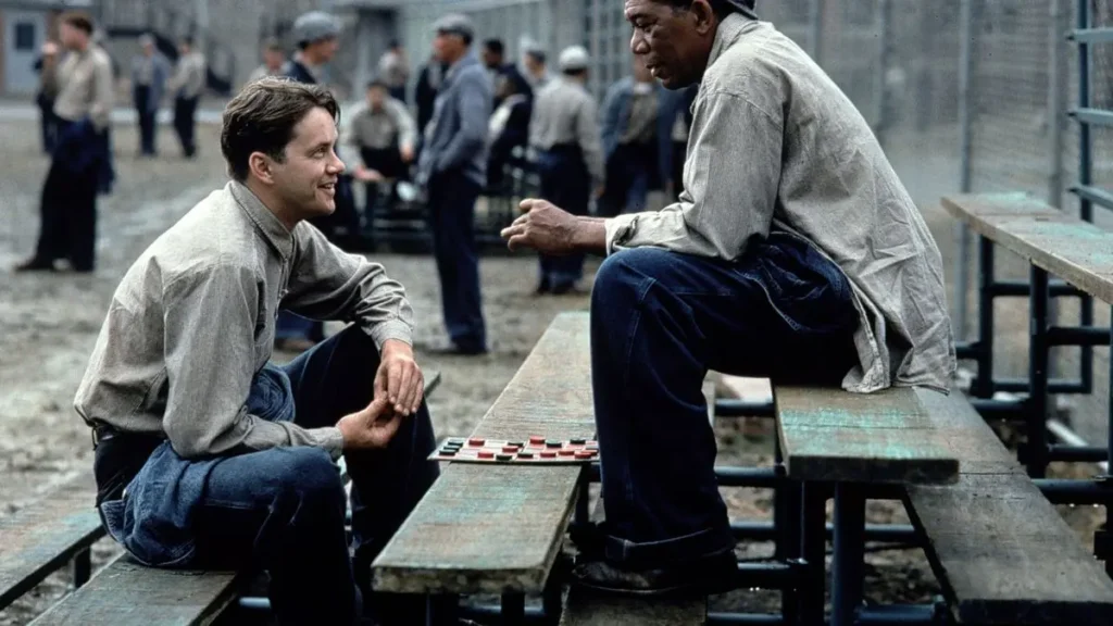 Andy Dufresne a Red si užívají volný čas během vězeňské pauzy, zatímco hrají dámu na dřevěných lavicích.