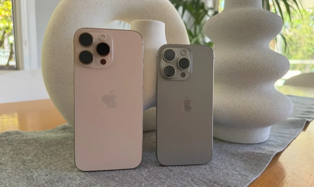 Dva modely iPhone 16 Pro vedle sebe – růžový a šedý, na pozadí dekorativní vázy