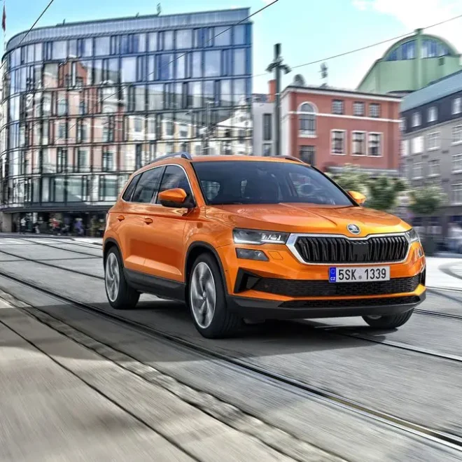 Škoda Karoq oranžové barvy projíždí městem po tramvajových kolejích, v pozadí moderní i historická architektura.