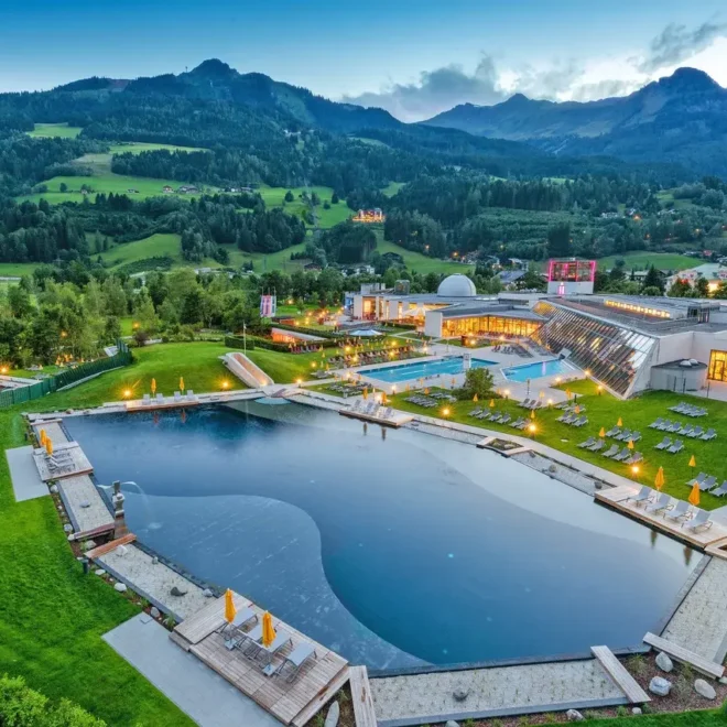 Termální lázně Alpentherme Gastein v Rakousku, obklopené alpskou přírodou. Noční osvětlení bazénů a venkovní relaxační zóny vytvářejí kouzelnou atmosféru pro relaxaci s výhledem na malebné hory v pozadí.