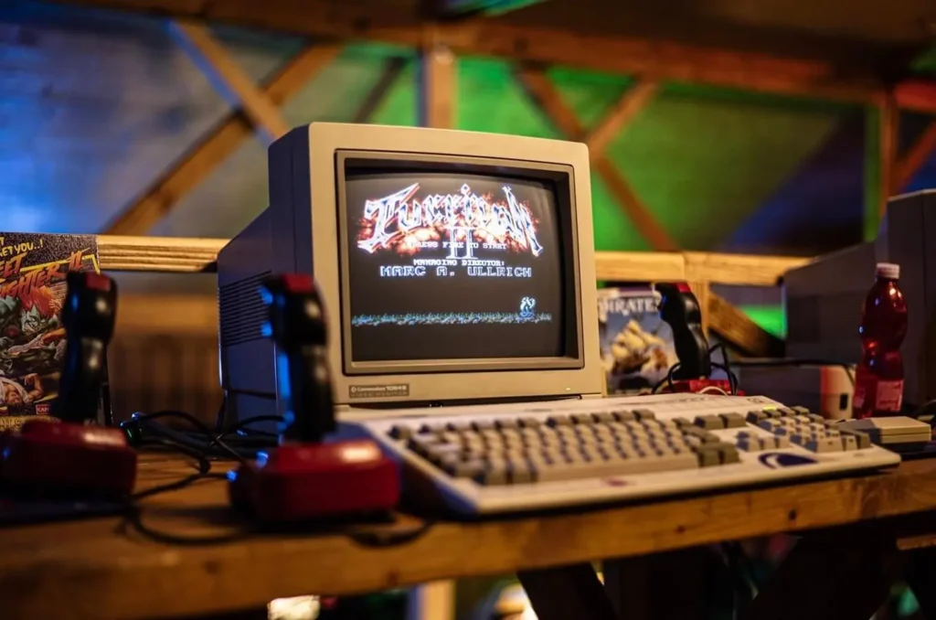 Retro počítač Commodore Amiga 1200 s CRT monitorem zobrazujícím hru Turrican II, joystickem a herními doplňky, připomínající atmosféru 80. a 90. let.