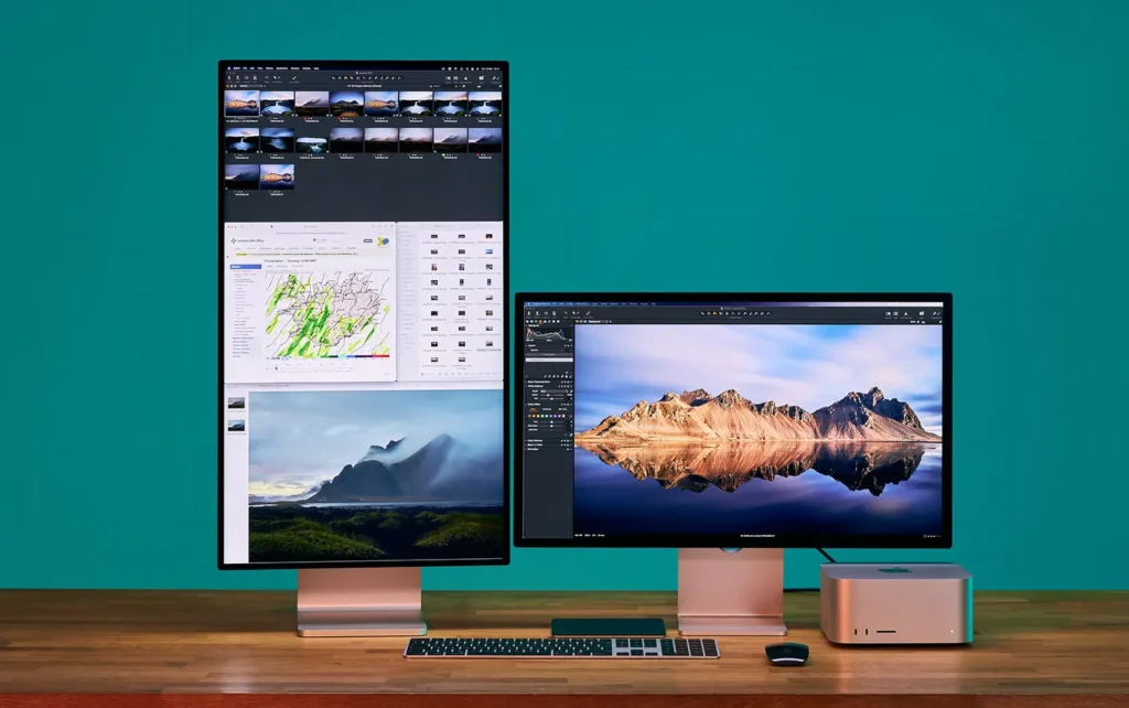 Apple Mac Studio a dva Studio Display monitory, z nichž jeden je orientován na výšku a druhý na šířku, umístěné na dřevěném stole s bezdrátovou klávesnicí a myší. Setup v moderním a čistém designu, vhodný pro profesionální tvůrce.