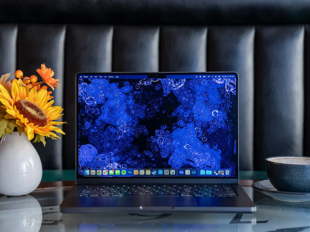 MacBook Pro M4 otevřený na stole, s detailním Mini-LED displejem a dekorací v podobě slunečnice a šálku kávy vedle zařízení.