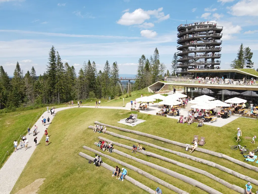 Restaurace s venkovním posezením a panoramatickou vyhlídkou v Bachledce. Návštěvníci relaxují a užívají si výhled na okolní přírodu a vyhlídkovou věž v pozadí.