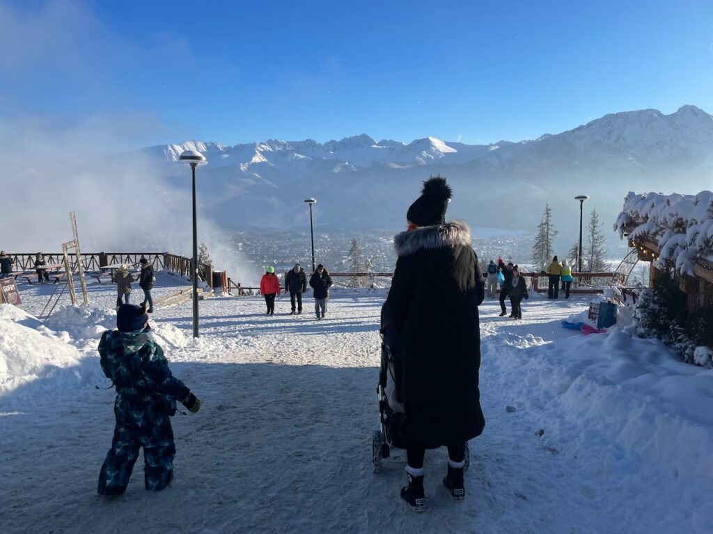 Lidé na vrcholu Gubałówky obdivující krásný výhled na zasněžené hory Tater a město Zakopane.