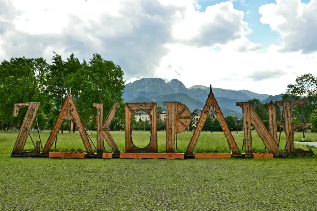 Dřevěný nápis 'Zakopane' v parku Rówień Krupowa s horami v pozadí, Zakopané, Polsko.