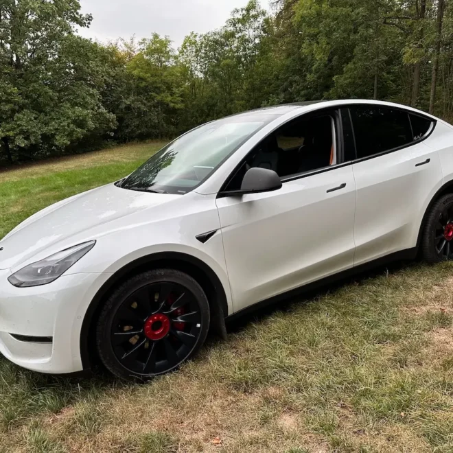 Bílá Tesla Model Y Performance s 21" Uberturbine koly zaparkovaná na travnaté ploše obklopené stromy.