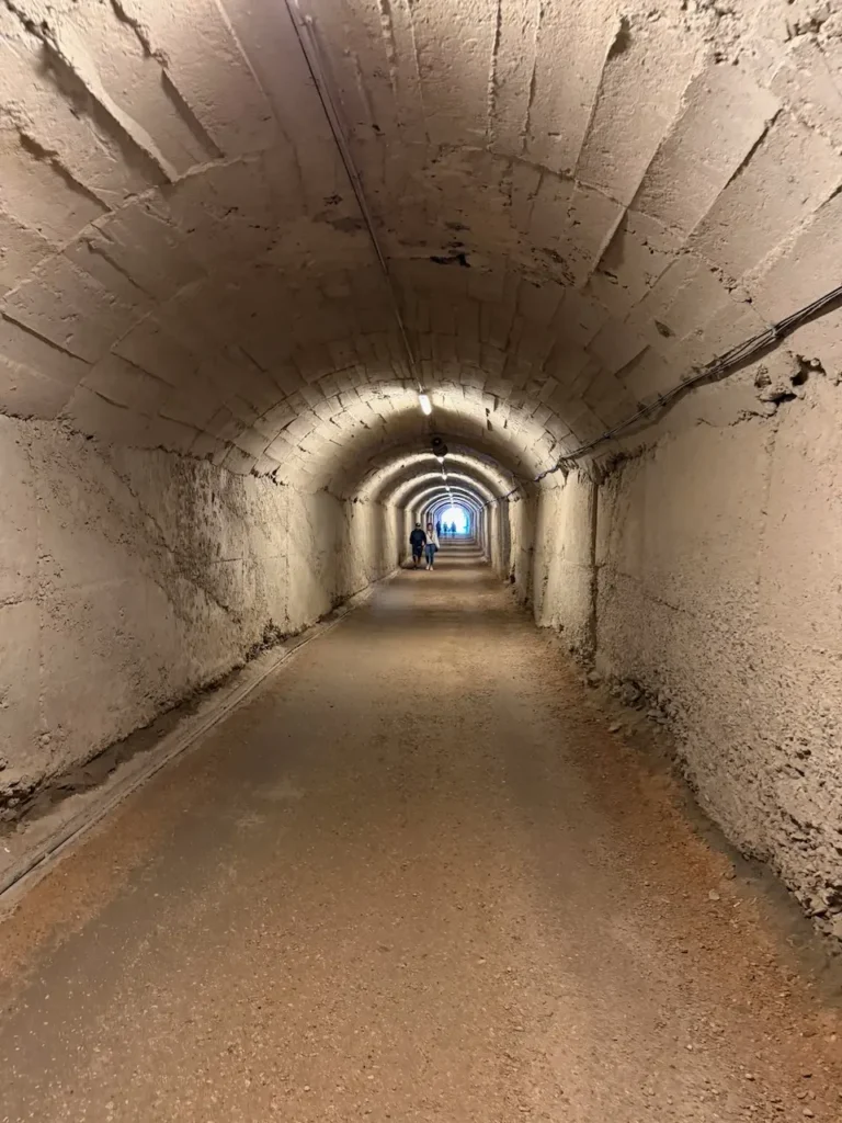 Dlouhý, betonový tunel vedoucí do nitra bunkru Bunk'Art 1 s viditelnými návštěvníky v dáli.