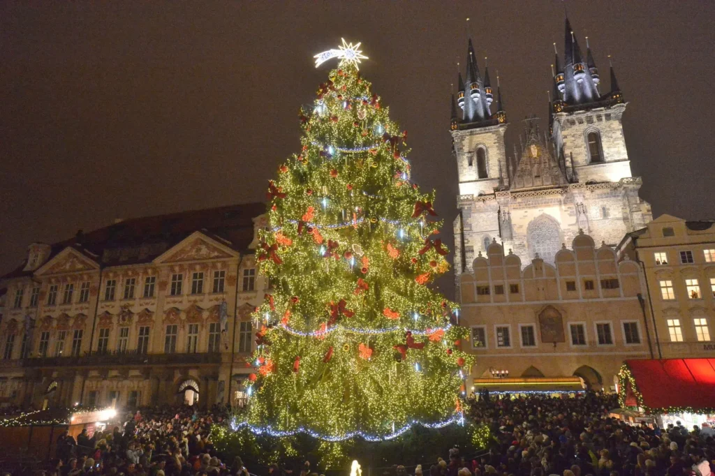 Slavnostně ozdobený vánoční strom na Staroměstském náměstí v Praze, obklopený historickými budovami a davem návštěvníků, kteří si užívají adventní atmosféru.