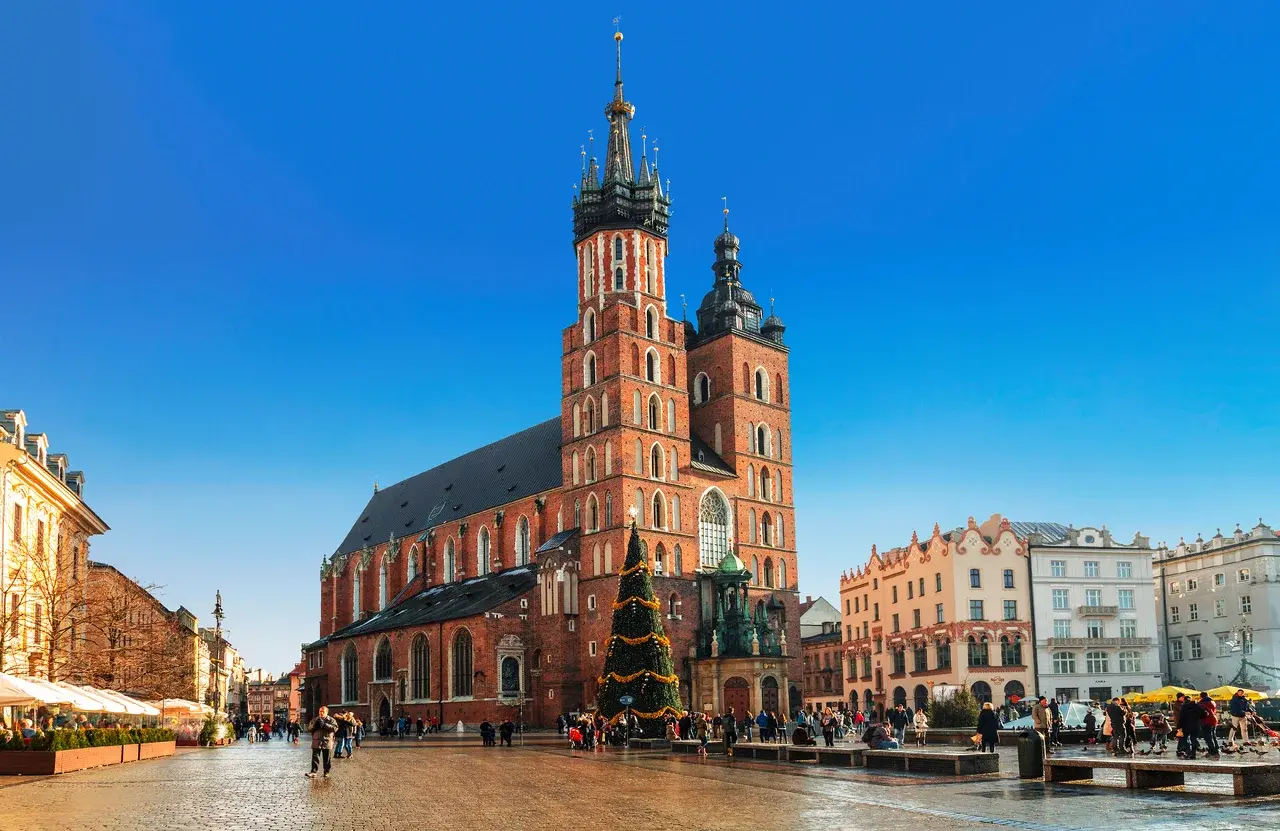 Vánoční trhy na hlavním náměstí Rynek Główny v Krakově, ozdobené vánočním stromem před historickými budovami a katedrálou.