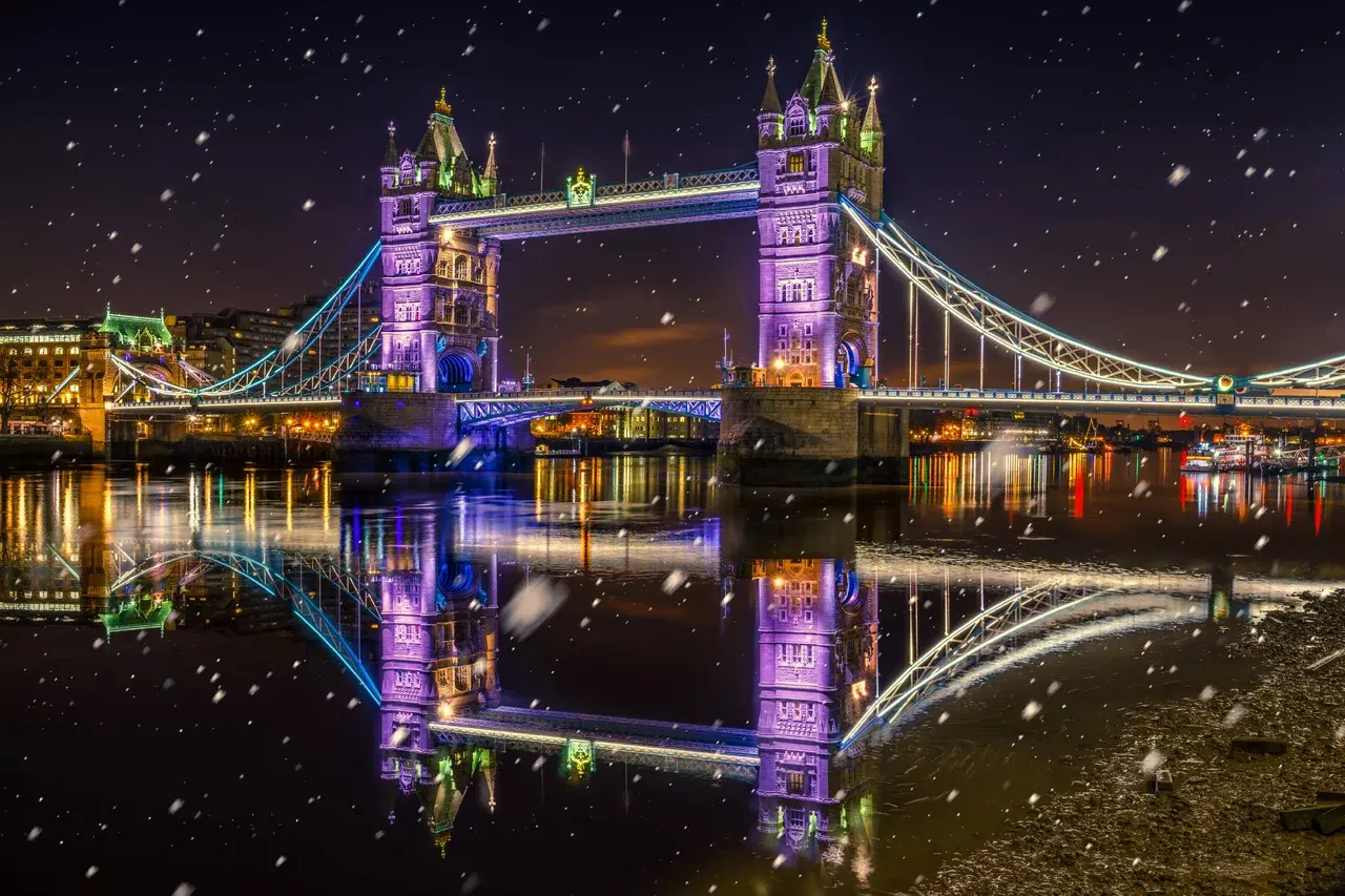 Tower Bridge v Londýně ve slavnostním vánočním osvětlení během adventní sezóny, zachycený v noci se sněhovými vločkami.