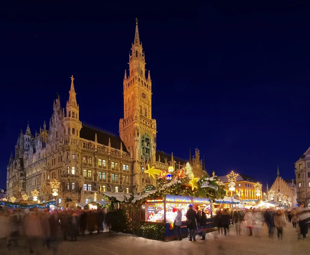 Pohled na vánoční trhy na Marienplatz v Mnichově, s osvětlenými stánky a historickou budovou Nové radnice v pozadí.