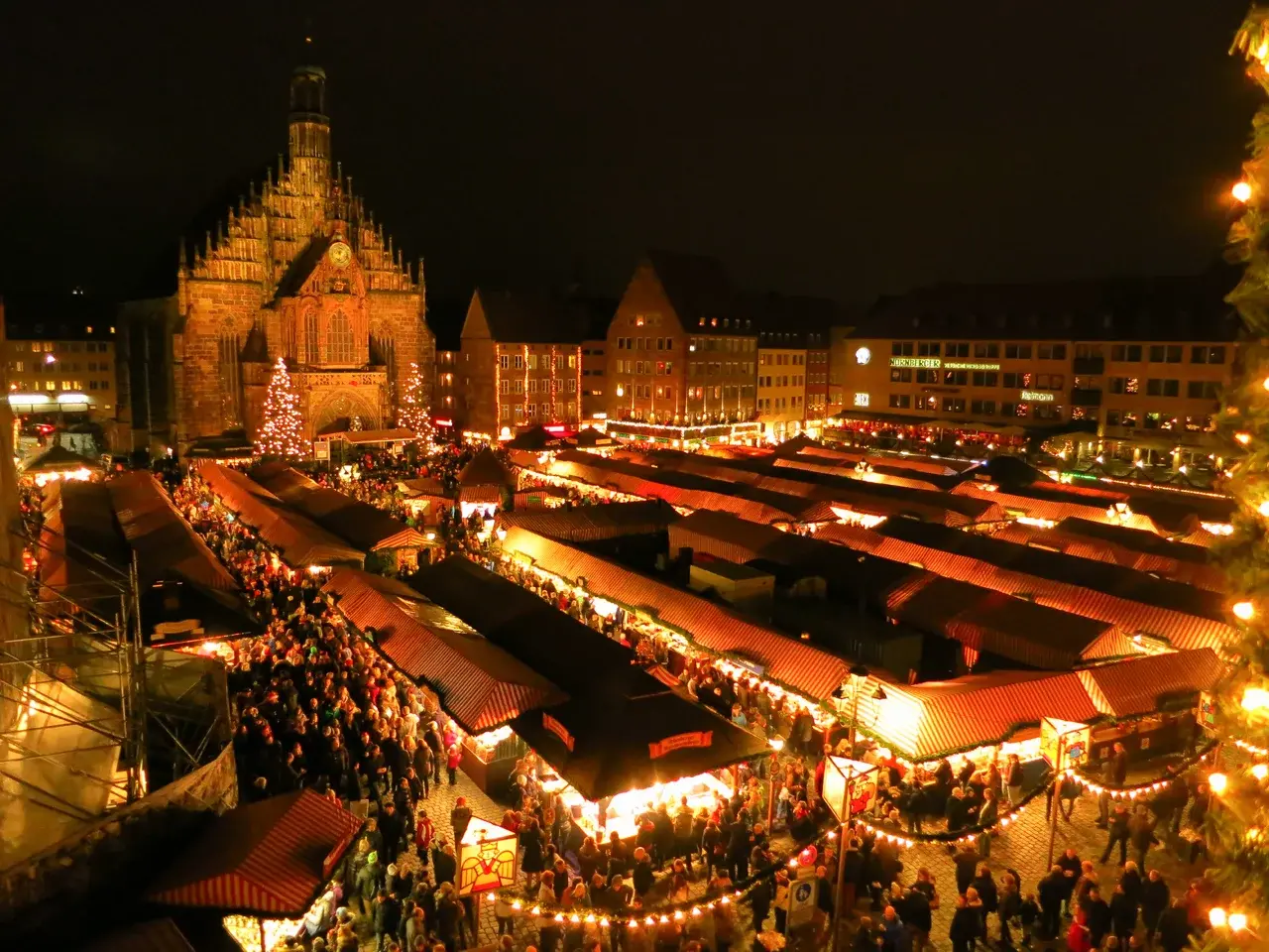 Vánoční trhy Christkindlesmarkt na náměstí Hauptmarkt v Norimberku, s vánočními stánky osvětlenými svíčkami v historickém centru města.