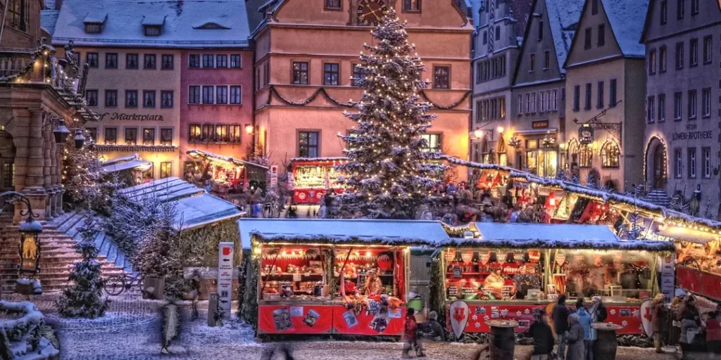 Adventní trhy v německém městě Rothenburg ob der Tauber, s osvětleným vánočním stromem, zasněženými stánky a historickou architekturou v pozadí.