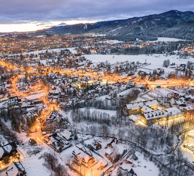 Zimní pohled na město Zakopané, Polsko – zasněžené domy, osvětlené ulice a panorama hor na pozadí.