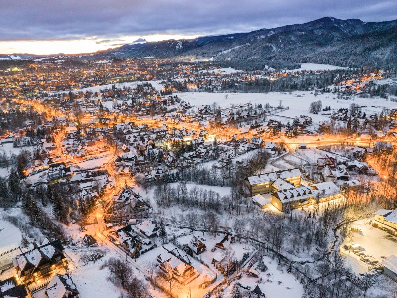 Zimní pohled na město Zakopané, Polsko – zasněžené domy, osvětlené ulice a panorama hor na pozadí.