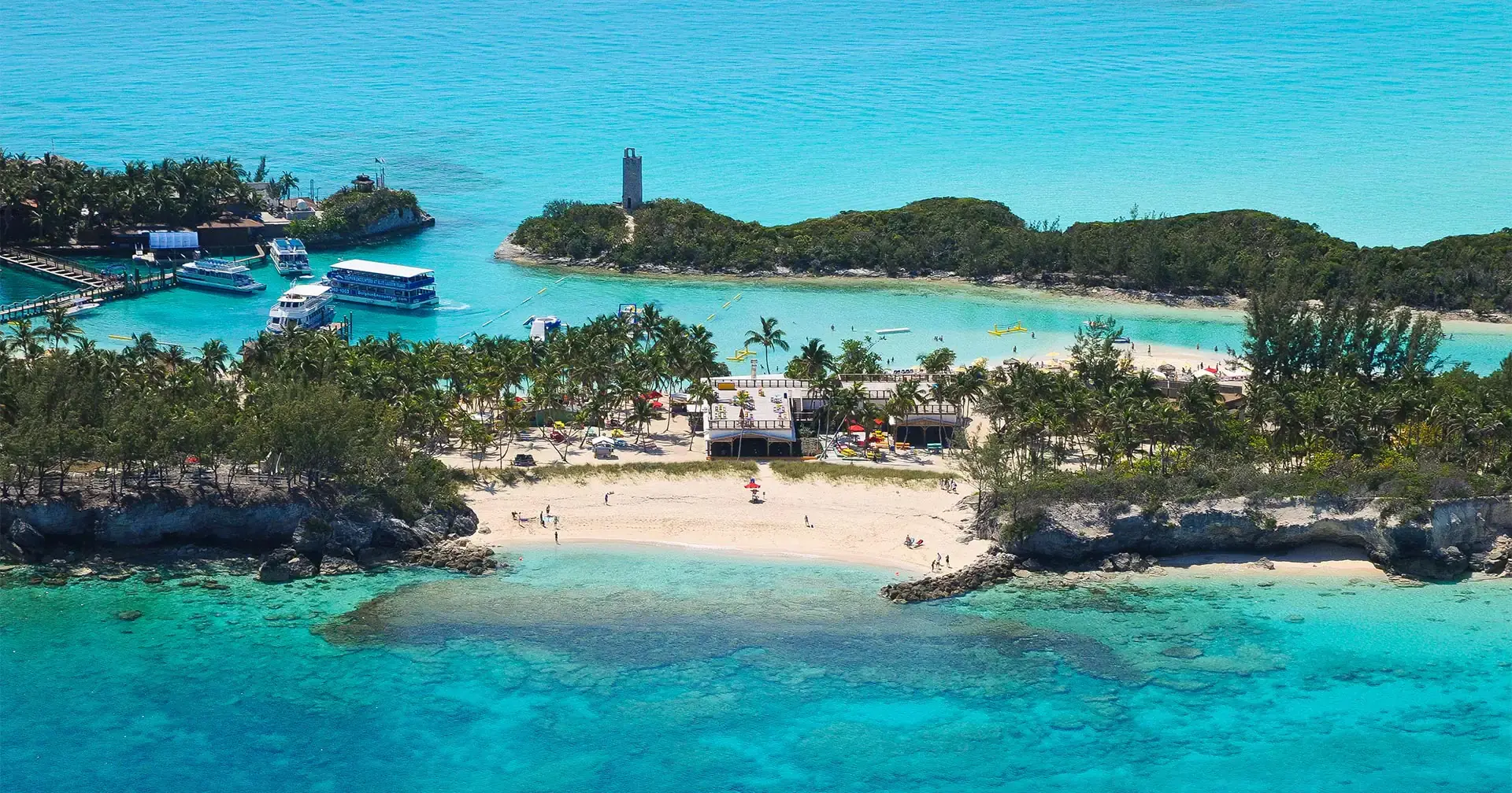 Letecký pohled na Blue Lagoon Island poblíž Nassau na Bahamách s tyrkysovou vodou, bílou pláží a loděmi kotvícími u přístavu.