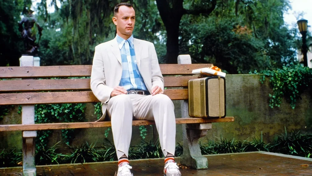 Tom Hanks jako Forrest Gump sedící na lavičce s kufříkem, známá scéna z filmu Forrest Gump.