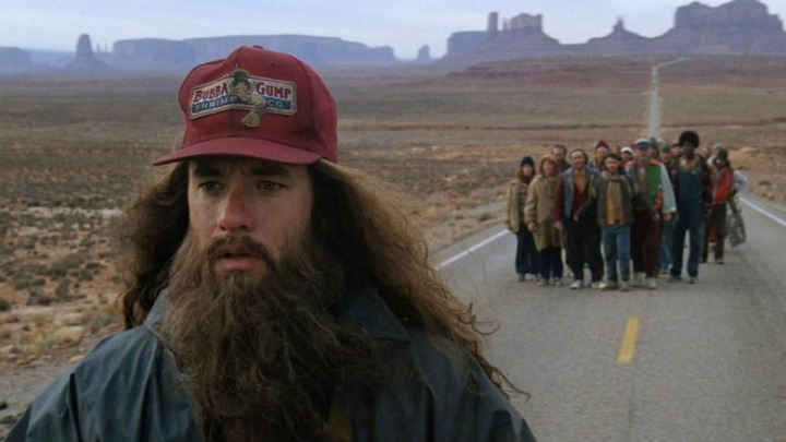 Scéna z filmu Forrest Gump, kde Tom Hanks s dlouhými vlasy a čepicí Bubba Gump Shrimp běží po silnici následován skupinou lidí.