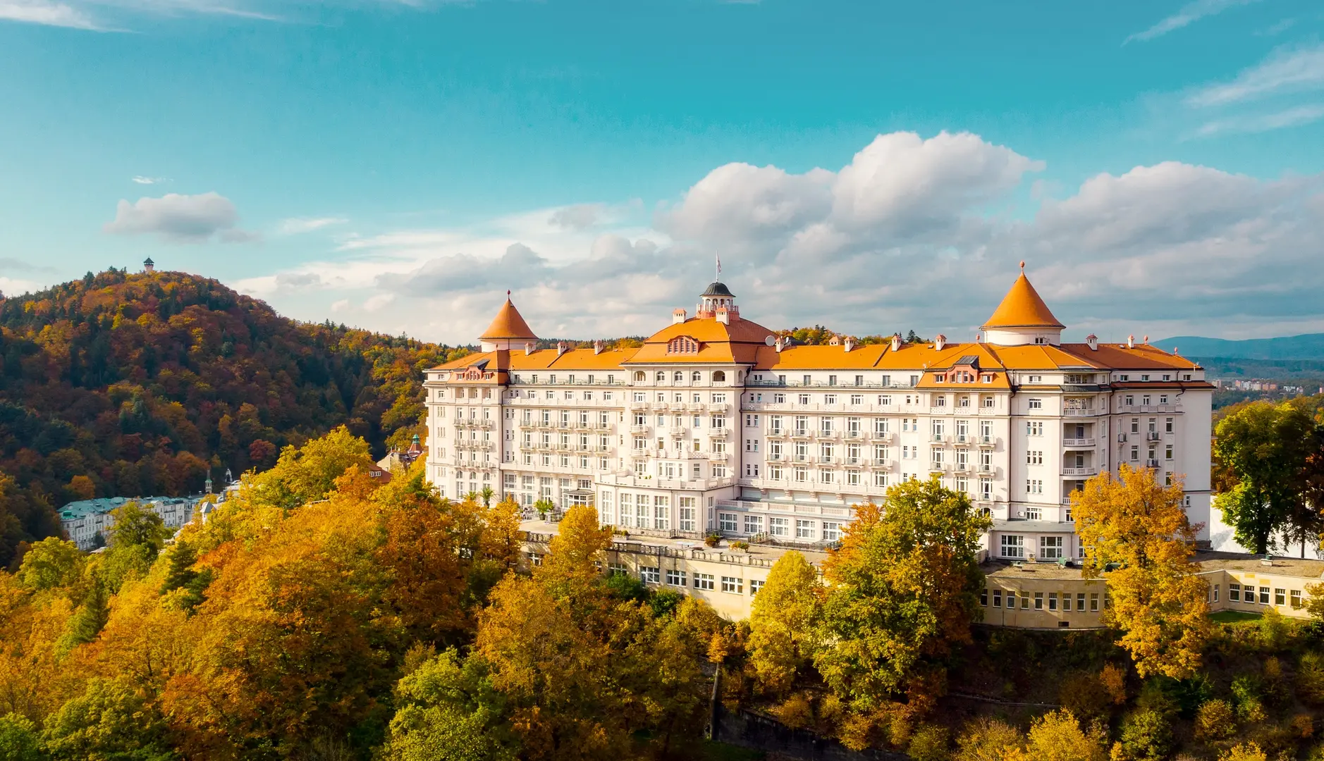 Hotel Imperial v Karlových Varech obklopený podzimní přírodou s výhledem na zalesněné kopce.