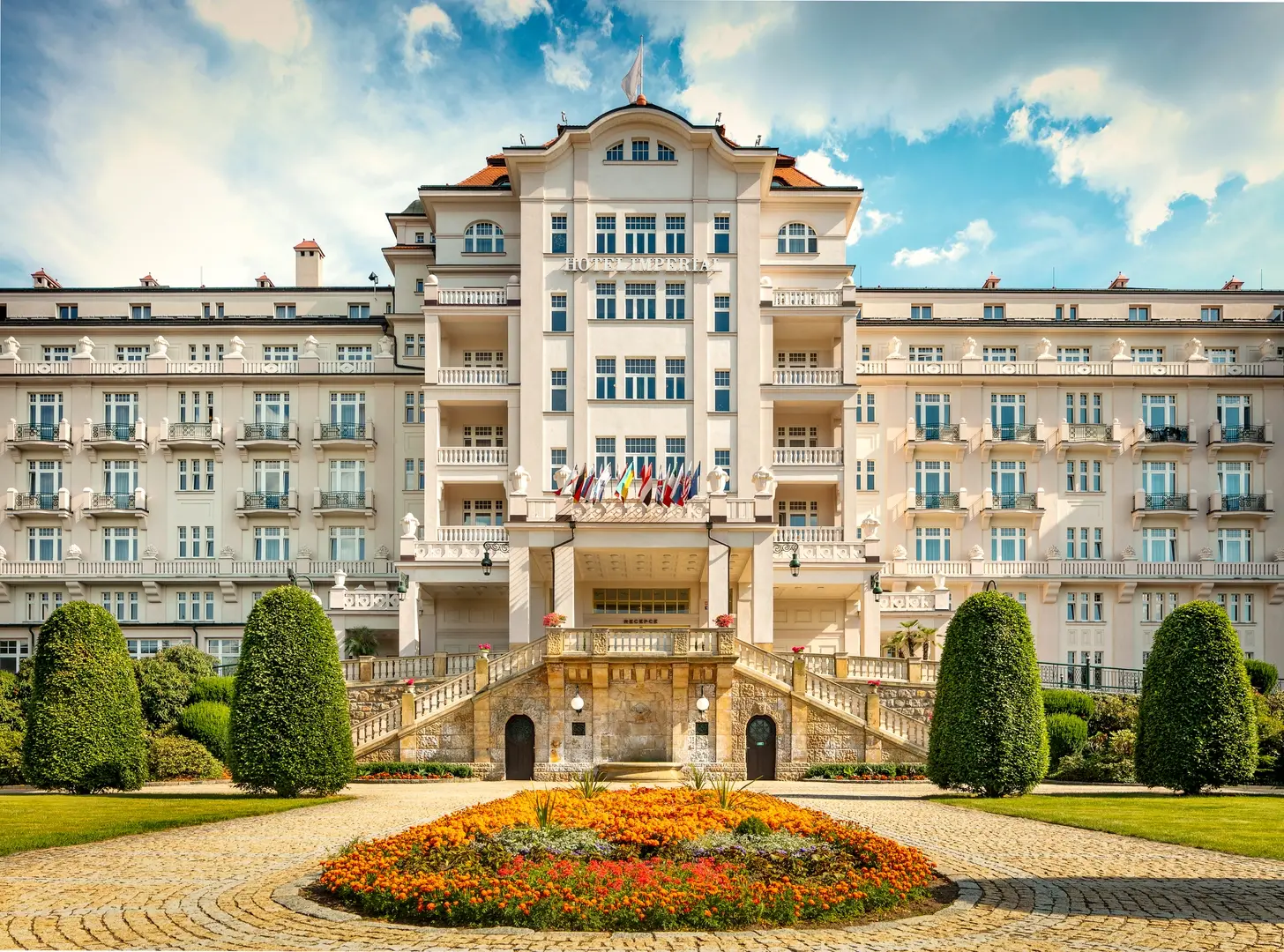 Čelní pohled na Hotel Imperial v Karlových Varech s květinovým záhonem.