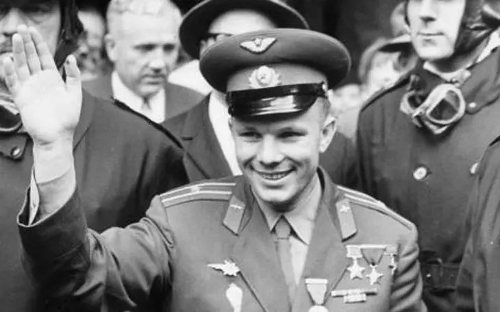 Jurij Gagarin v uniformě sovětského letectva s medailemi na hrudi, mávající davu s úsměvem na tváři. Fotografie zachycuje Gagarina po jeho triumfálním návratu na Zemi jako prvního člověka, který se dostal do vesmíru.