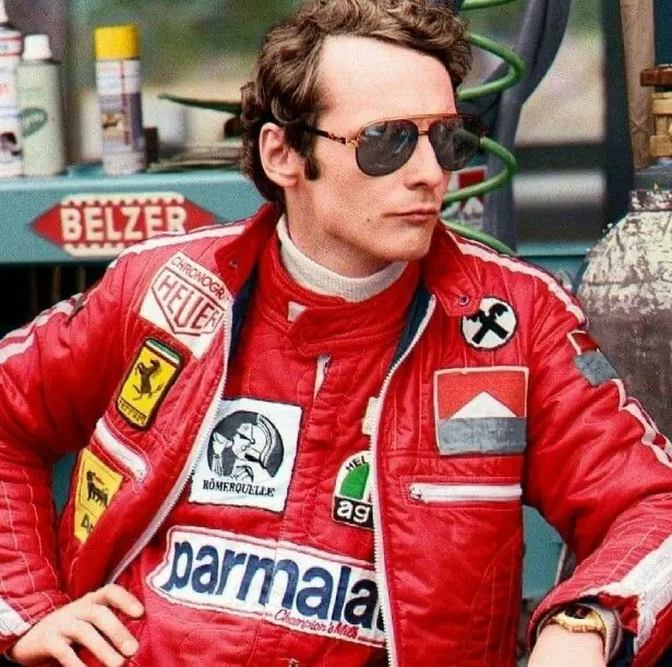 Niki Lauda ve své červené kombinéze Ferrari, s brýlemi a typickým profesionálním výrazem během závodní pauzy.