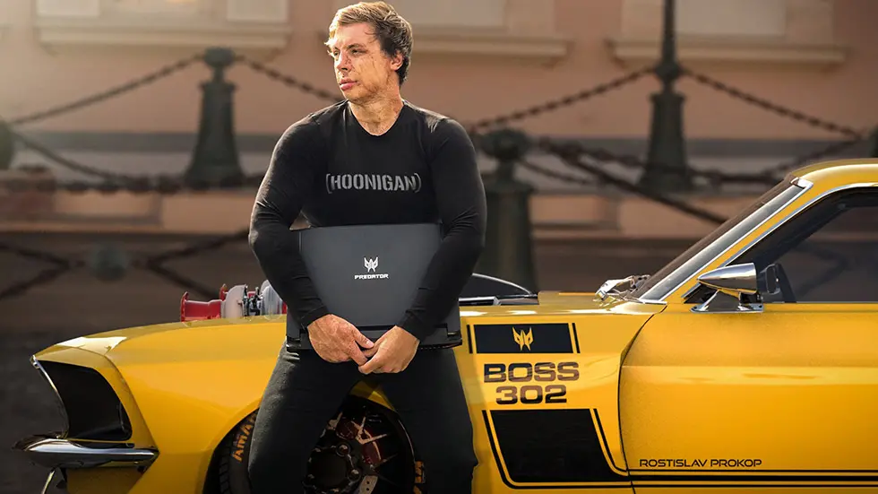 Rostislav Prokop, český automobilový designér, stojí vedle svého upraveného Fordu Mustang Boss 302 v černém tričku s nápisem HOONIGAN a drží notebook Acer Predator.