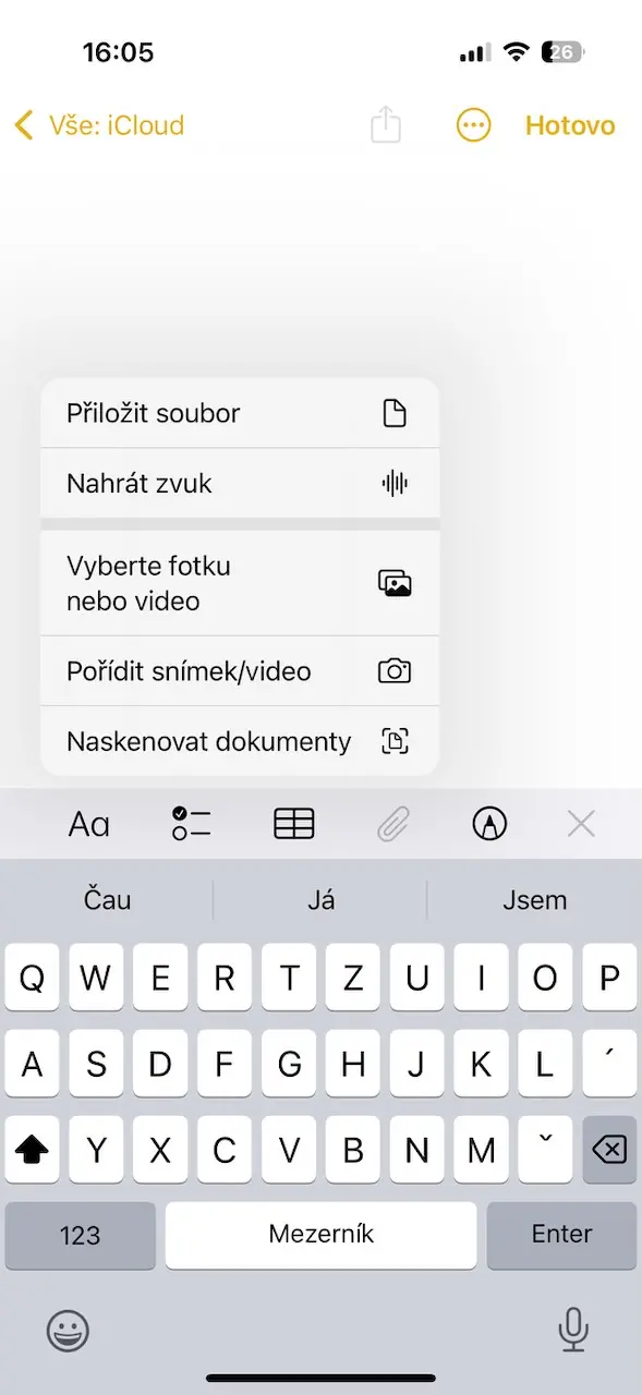 Záznam z aplikace Poznámky na iPhone. Otevřená klávesnice s nabídkou možností přidání souboru, nahrání zvuku, výběru fotografie nebo videa, pořízení snímku/videa a skenování dokumentů.