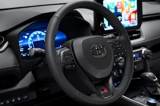 Detailní pohled na volant a palubní desku Toyoty RAV4 s integrovanou dotykovou obrazovkou a digitálním tachometrem.