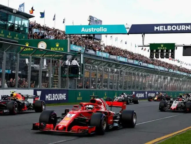 Startovní rošt Velké ceny Austrálie Formule 1 v Melbourne s červeným vozem Ferrari na čele, obklopeným dalšími monoposty, zatímco diváci sledují závod z tribun.