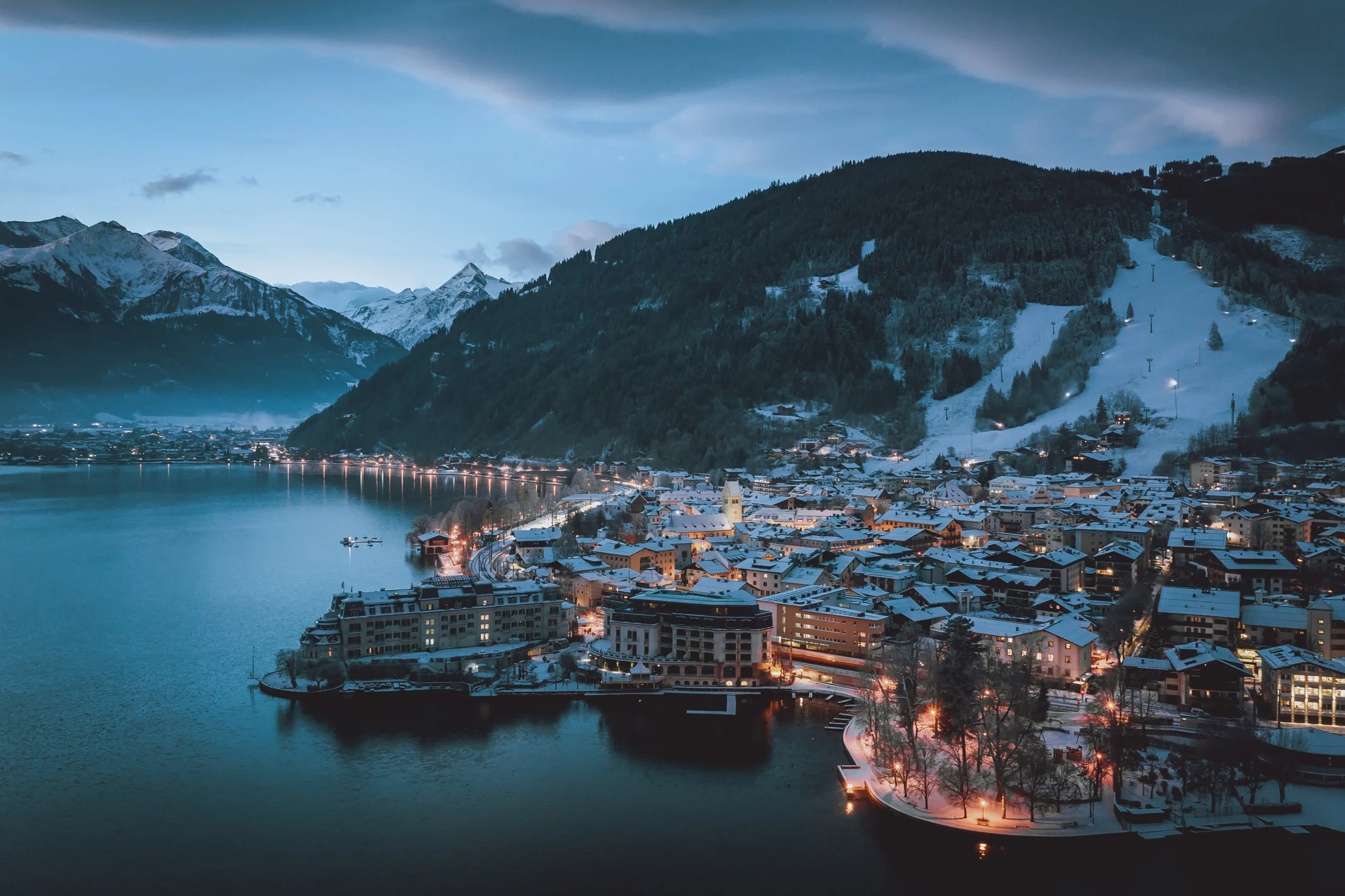 Pohled na noční město Zell am See s osvětlenými svahy a jezerem v zimní atmosféře.