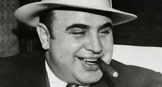 Al Capone se širokým úsměvem a doutníkem v ústech, typická scéna zachycující legendárního mafiánského bosse.