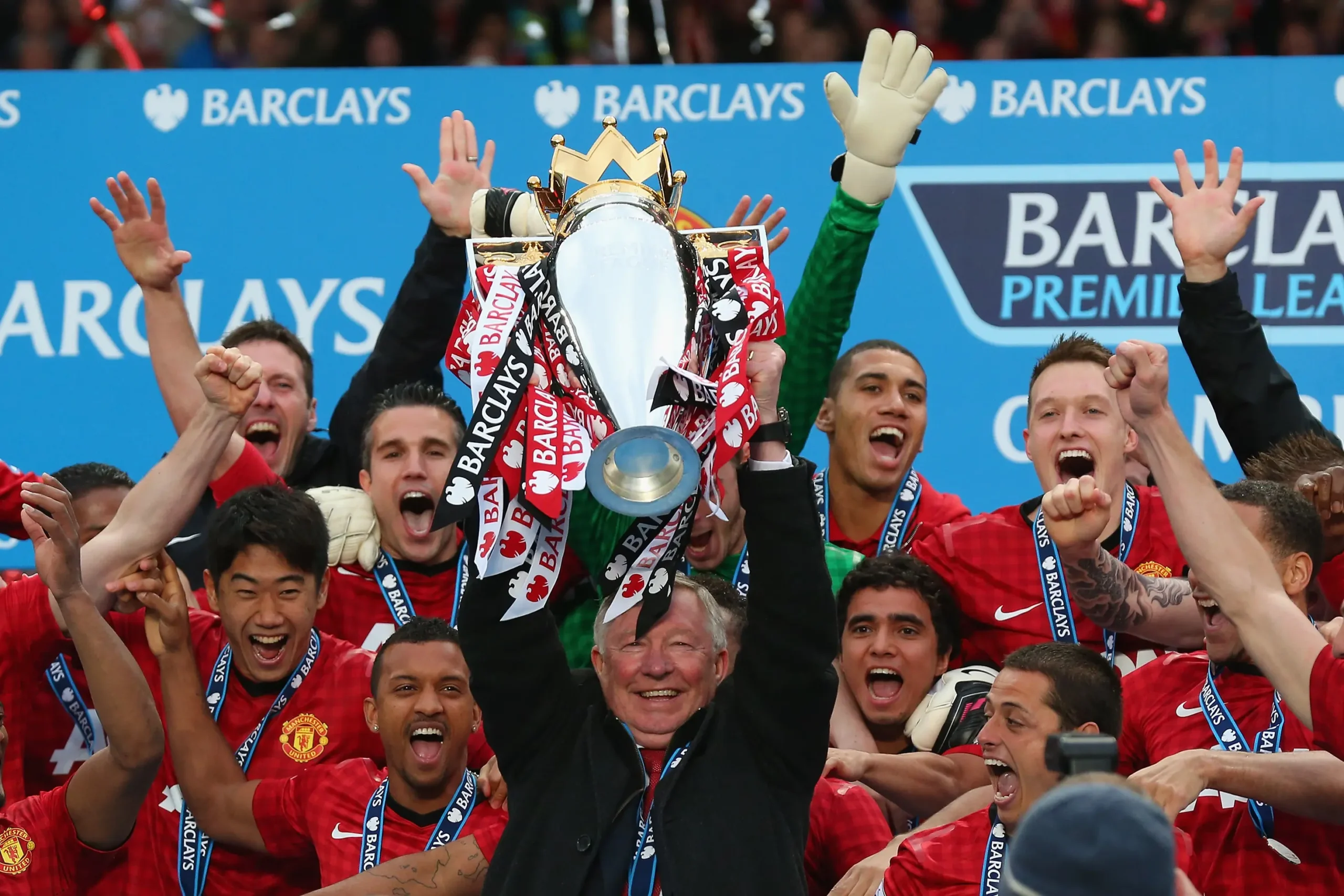 Alex Ferguson drží trofej Premier League obklopený hráči Manchester United při oslavách vítězství.