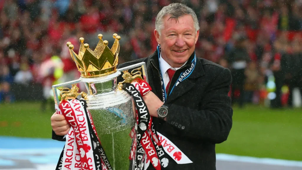 Alex Ferguson s trofejí Premier League, symbolizující jeho úspěšnou trenérskou kariéru.