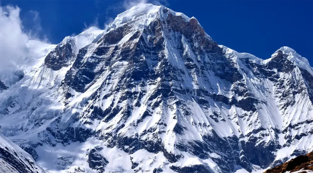 Monumentální zasněžená stěna hory Annapurna I, desáté nejvyšší hory světa, pod jasnou modrou oblohou.