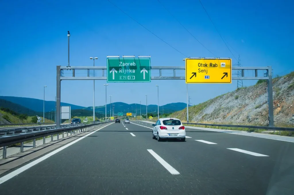 Chorvatská dálnice vedoucí k městům Záhřeb a Rijeka s jasným značením směru a odbočkou na ostrov Rab a město Senj, dopravní situace za slunečného dne s projíždějícími auty.