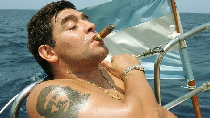 Maradona odpočívá na lodi s doutníkem, symbolizující jeho životní styl a vášeň pro neapolskou i argentinskou kulturu.