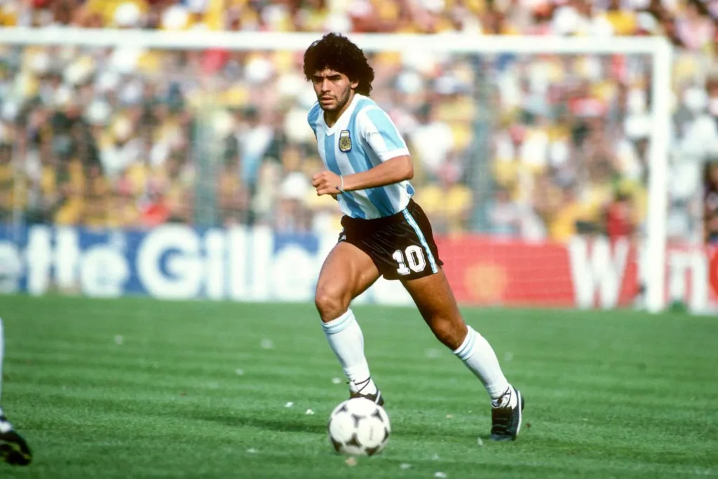 Diego Maradona mladý v dresu argentinské reprezentace – Mladý Diego Maradona dribluje s míčem během zápasu mistrovství světa, typický obraz jeho neuvěřitelné fotbalové techniky.