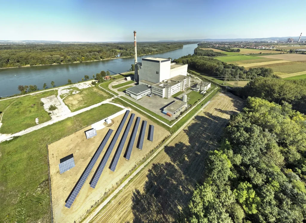 Letecký pohled na areál jaderné elektrárny Zwentendorf v Rakousku, obklopený solárními panely a řekou Dunaj v pozadí.