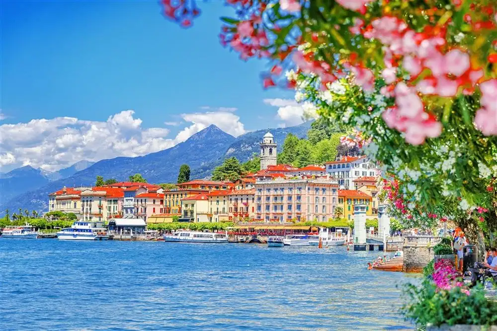 Barevné městečko u jezera Lago di Como s rozkvetlými květinami a modrou hladinou.