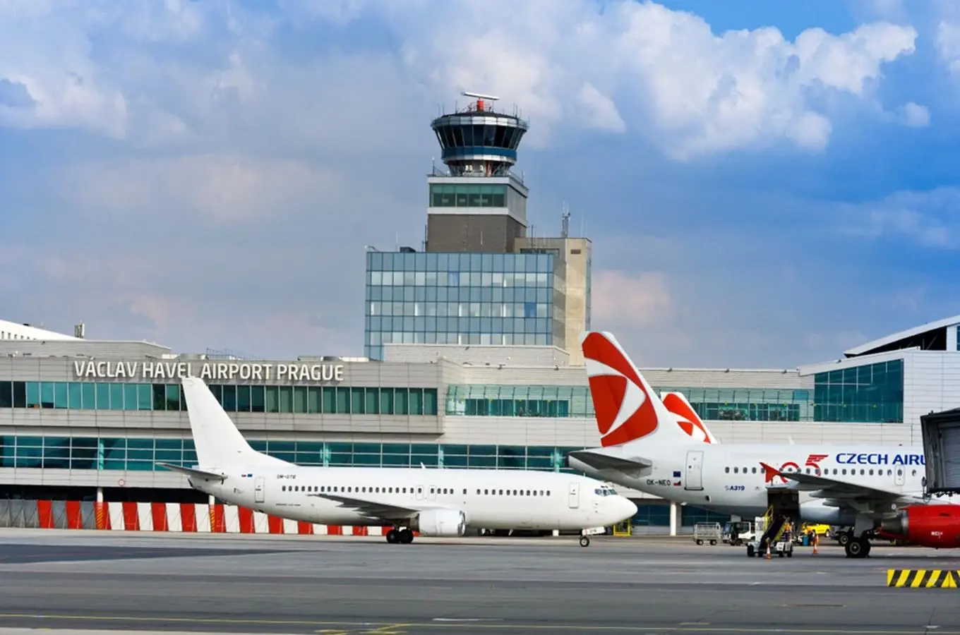 Letištní plocha na Letišti Václava Havla v Praze s odbavovací halou, řídicí věží a zaparkovanými letadly Českých aerolinií.