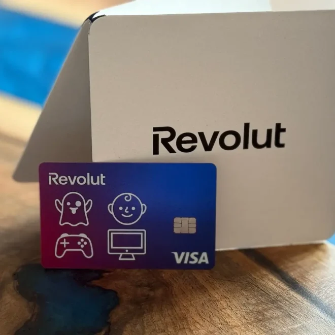 Revolut platební karta s hravými ikonami položená před elegantním bílým obalem s logem Revolut, zachyceno na stylovém dřevěném stole.