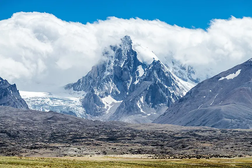 Vrchol hory Šiša Pangma v Tibetu, obklopený ledovci a zahalený částečně v oblacích.