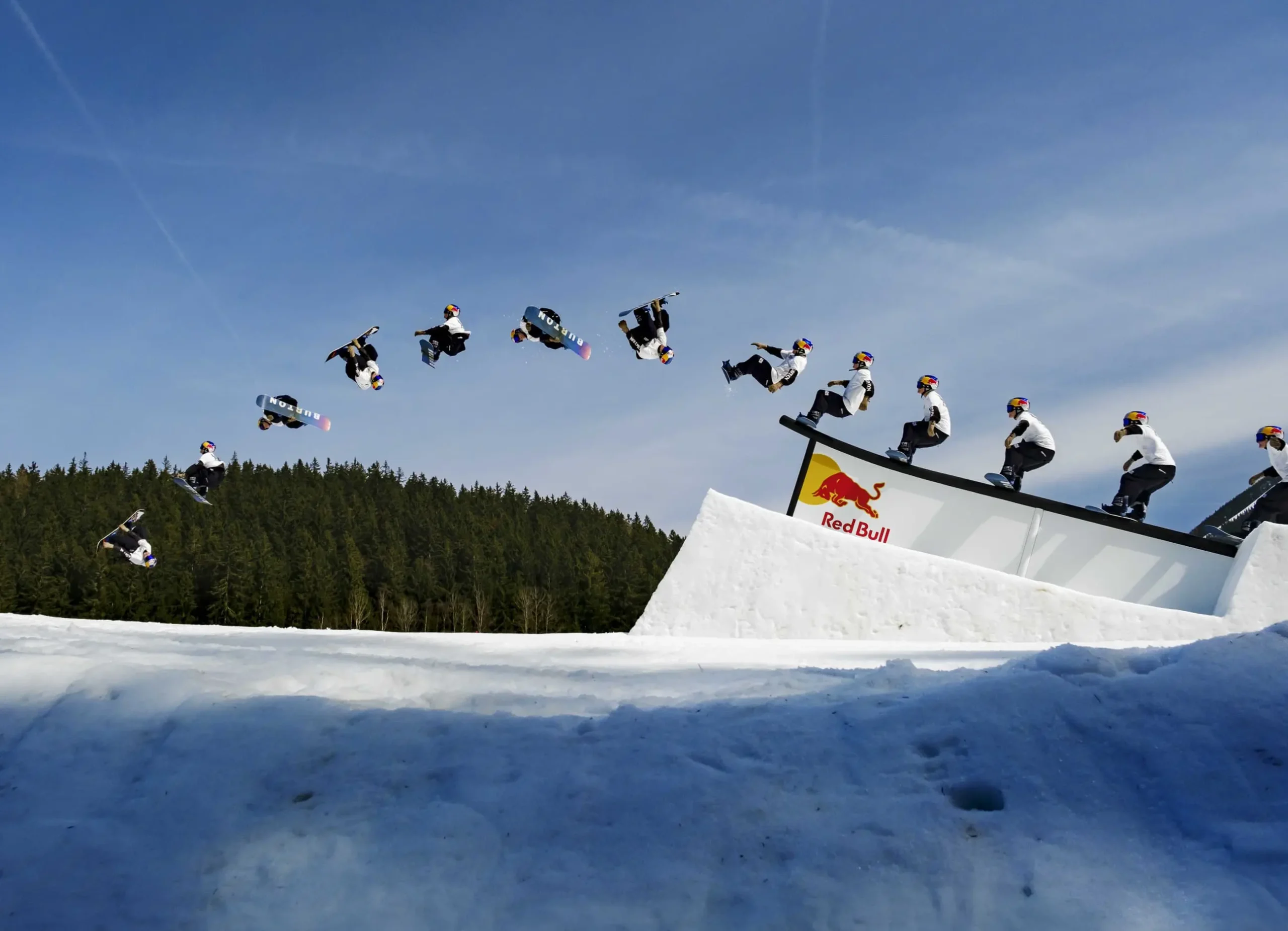 Profesionální snowboardista předvádí sekvenci skoků a triků na snowparku s logem Red Bull.