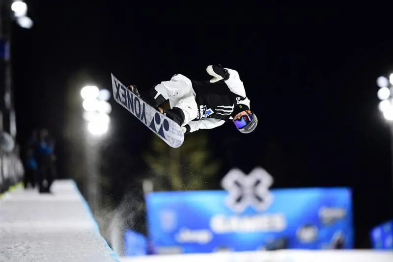 rofesionální snowboardista předvádějící trik během soutěže na Winter X Games v noci.