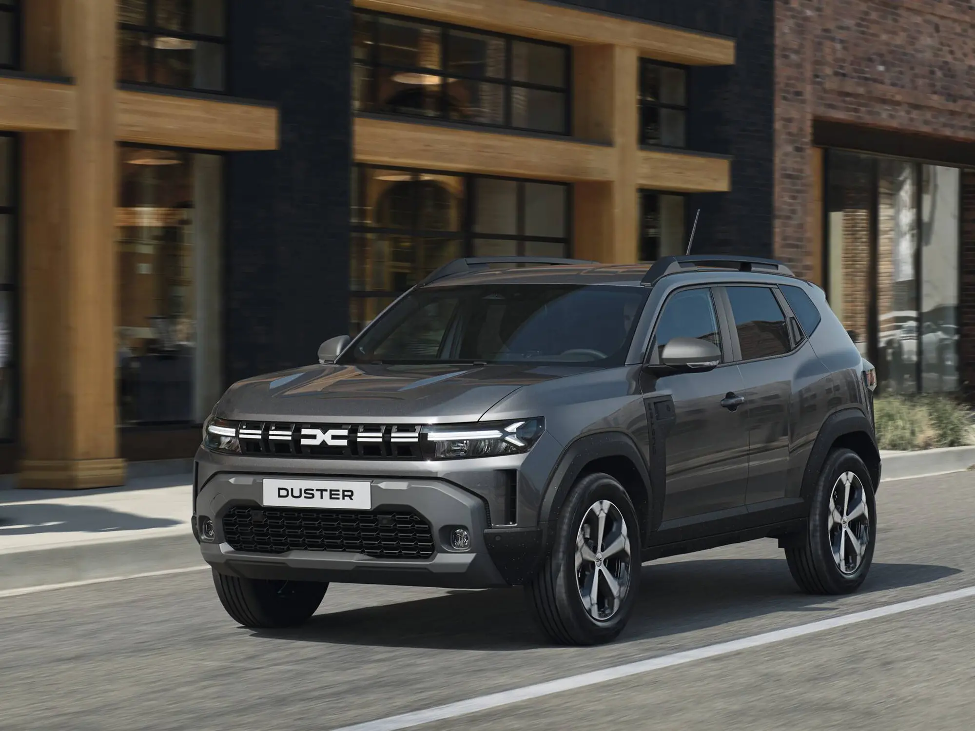 Dacia Duster 2024 v městském prostředí, pohled zepředu na nové světlomety, masivní masku chladiče a elegantní linie SUV.