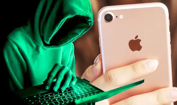 Hacker v zelené mikině s kapucí pracující na notebooku vedle osoby držící iPhone, symbolizující možný hackerský útok na zařízení Apple.