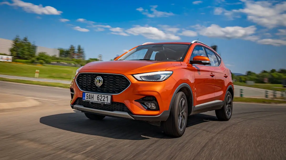 Oranžové MG ZS při dynamické jízdě po městské silnici. Výrazná maska chladiče a sportovní design dodávají vozu energický vzhled.